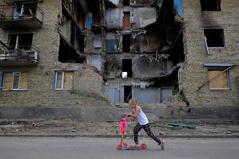 Tyttö potkulautailee tuhoutuneen asuinrakennuksen ohi Horenkan kylässä Kiovan alueella 4. kesäkuuta 2022.