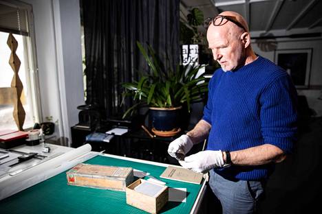 Petri Nuutinen käsittelee työhuoneellaan vanhoja lasinegatiiveja asiaankuuluvan varovaisesti. Osa kuvista on edelleen taidemaalari Aira Hellaakosken käyttämissä väriliitulaatikoissa.