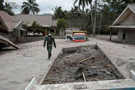 Indonesialainen sotilas kävelee vaurioituneiden kuorma-autojen ohi Sumberwuluhin kylässä Indonesiassa sen jälkeen, kun Semeru-tulivuori purkautui. Kuva on otettu 5. joulukuuta 2021.