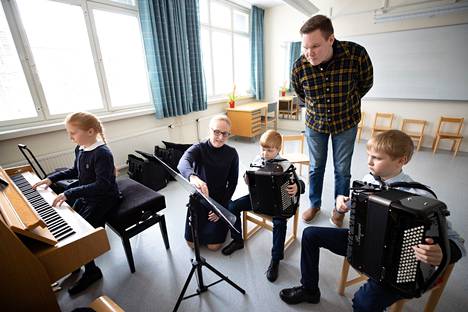 Minimuusikoiden duo on kasvanut trioksi, kun Annabel ja Samuel Heikolan seuraan on liittynyt esityksissä Rafael-pikkuveli. Eriikka-äiti ja harmonikansoiton opettaja Pasi Raukola ohjaavat lapsia soittoharjoituksessa.