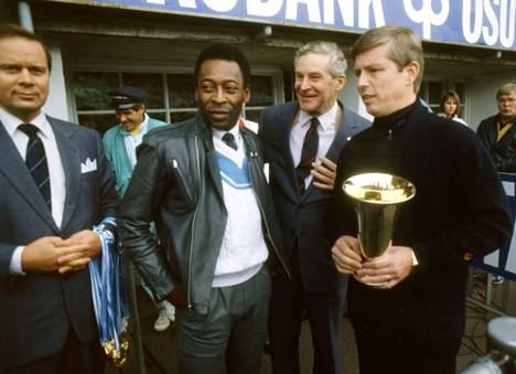 Brasilialainen jalkapallon pelaaja Pelé Suomessa 21. syyskuuta 1986. Pele jakaa palkinnot mimmiliigan mestareille HJK:n naisille HJK–Kuusysi-ottelun jälkeen stadionilla. Palkintopokaali on toimittaja Janne Virkkusen käsissä.