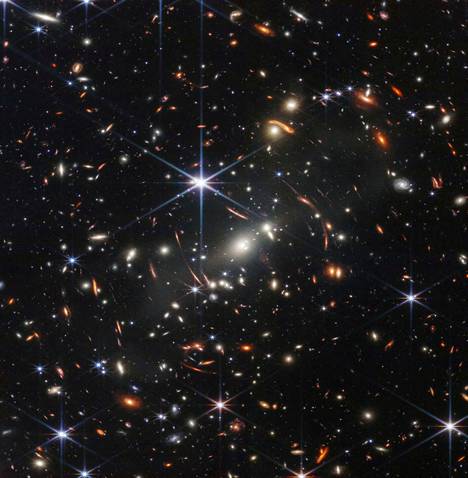 Avaruusteleskooppi James Webbin ensimmäinen julkaistu värikuva. Se on galaksijoukosta SMACS 0723 ja sen takaa. Kuvan punertavat  kaaret ja pallukat ovat säteilyä galakseista hyvin varhaisessa universumissa. Webbin tarkka kamera NIRCam toi nämä galaksit näkyviin ensi kertaa. Niissä on säteilyä, joka on lähtenyt matkaan selvästi yli 13 miljardia vuotta sitten. 