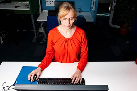 Työterveyslaitoksen erityisasiantuntija Elina Östring näyttää oikeanlaisia työskentelyasentoja tietokoneen ääressä. Käsien pitää saada tukea pöytätasosta.