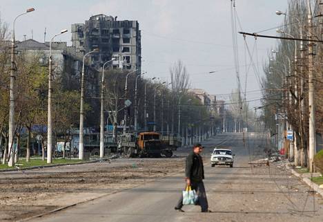 Mies ylitti katua Mariupolin kaupungissa perjantaina. Taustalla näkyy taisteluissa tuhoutunut rakennus.