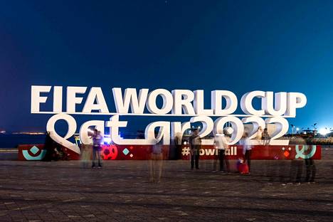 Turistit kuvaamassa itseään Dohassa Qatarissa järjestettävien jalkapallokisojen mainoksen alla.