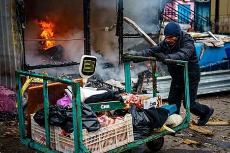 Mies kuljetti kärryä pommituksissa palamaan syttyneen kaupan edessä Hersonissa Ukrainassa 24. joulukuuta. 