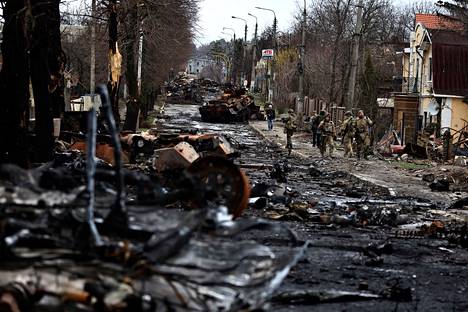 Ukrainalaiset sotilaat kävelivät venäläisten tuhoutuneen sotakaluston ohi Butšassa lauantaina. 