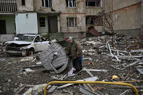 Iäkäs nainen seisoo raunioiden keskellä lähellä vahingoittunutta kerrostaloa Harkovan etulinjalla. Kuva on otettu 27.3.2022.