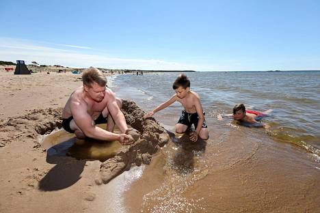 Juhani Nurmi (vasemmalla) ja Sisu Nurmi rakentavat hiekasta linnoitusta. Oskari Nurmi vilvoittelee meressä.