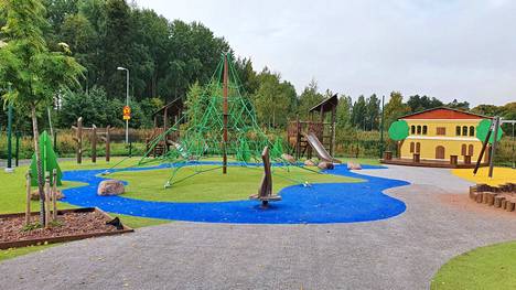 Klasipruukinpuiston leikkipaikan etualalla on kuusisakarainen pihakuusen mallinen verkkokiipeilyteline ja taustalla keltainen piharakennuksen julkisivuelementti.