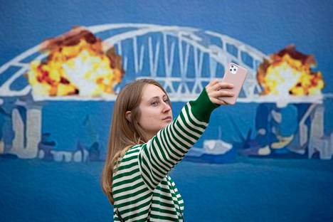 Nainen poseerasi Krimin pommitettua siltaa kuvaavan jättikokoisen postimerkkimallin edustalla Kiovassa lokakuussa. Ukraina pommitti siltaa lokakuun alussa.