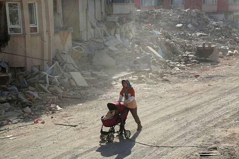 Lastenvaunuja työntävä nainen ohitti maanjäristyksen tuhoaman talon Adiyamanissa Turkissa sunnuntaina.