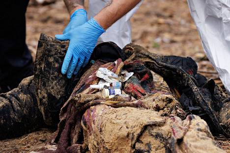Ukrainalaiset viranomaiset avaavat siviilien haudat ja joukkohaudat Izjumissa. Kuvassa tarkastetaan haudasta löytyneen ruumiin taskut.