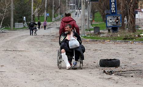 Nainen veti pyörätuolilla perässään haavoittunutta miestä Mariupolissa. 
