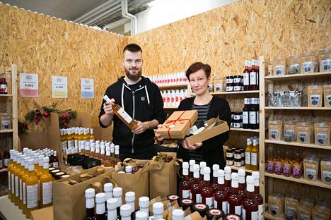 Nikolas Jokisalon kädessä on luomuglögiä ja Eeva Hakala kannattelee käsissään lahjapakettia. Tehtaanmyymälässä on saatavilla koko yrityksen tuotevalikoima. Siellä voi olla myös tuotekehittelyeriä ja poistotuotteita.