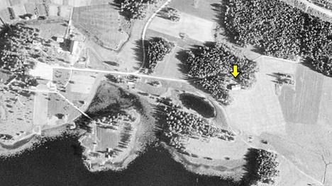 Vuonna 1951 otetussa ilmakuvassa vasemmalla Joenniemen kartanon piha-alue. Tilan rakennuksiin kuulunut heinälato on merkitty nuolella. Kuvan vaaleat alueet ovat enimmäkseen peltoja. Kuvalähde: Maanmittauslaitoksen historiallisten ilmakuvien arkisto.