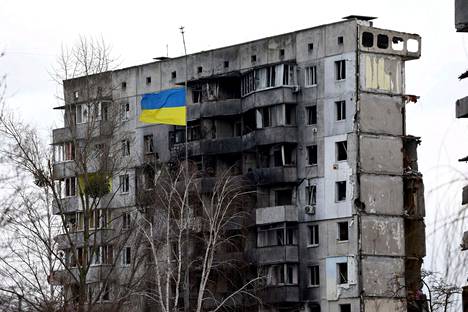 Ukrainan lippu liehui tuhoutuneen rakennuksen edessä Kiovan alueella 18. helmikuuta 2023.