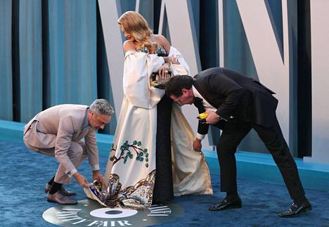 Oscar-iltana ohjaaja Taika Waititi (vas.) kyykistyi auttamaan Rita Oraa mekon kanssa. Taiteilijat olivat menossa Vanity Fair -lehden Oscar-juhliin. Oikealla nimettömäksi jäänyt pr-avustaja.