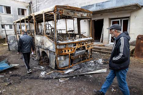 Miehet kävelevät raketin tuhoaman koulubussin ohi. Makarivin keskusta on kärsinyt raskaita tuhoja. 