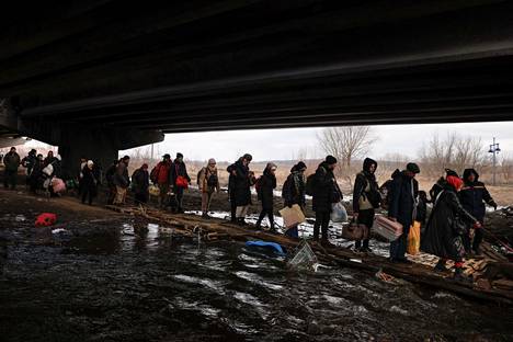 Ihmisiä pakenemassa Kiovan alueella sijaitsevasta Irpinin kaupungista 9. maaliskuuta. Ihmiset ylittävät jokea pitkospuiden päällä, sillä yllä oleva silta on tuhoutunut Venäjän hyökkäyksessä. 