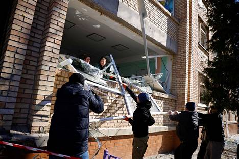 Ihmiset siivoavat rojua koulurakennuksesta lähellä pommituksessa osuman saanutta kerrostaloa Kiovassa perjantaina aamupäivällä.