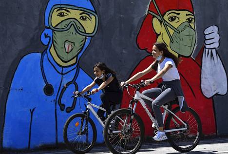 Kaksi tyttöä pyöräili korona-aiheisen muraalin edustalla Pohjois-Makedonian Skopjessa toukokuussa. Koronapandemia vaikuttaa monin tavoin lasten elämään eri puolilla maapalloa.