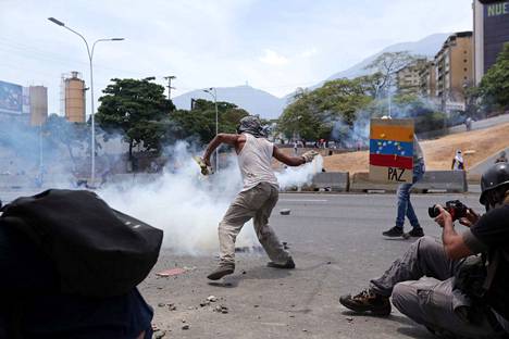 Mielenosoittaja heittää mellakkapoliisin ampuman kyynelkaasupatruunan takaisin Venezuelan pääkaupungissa Caracasissa keskiviikkona.