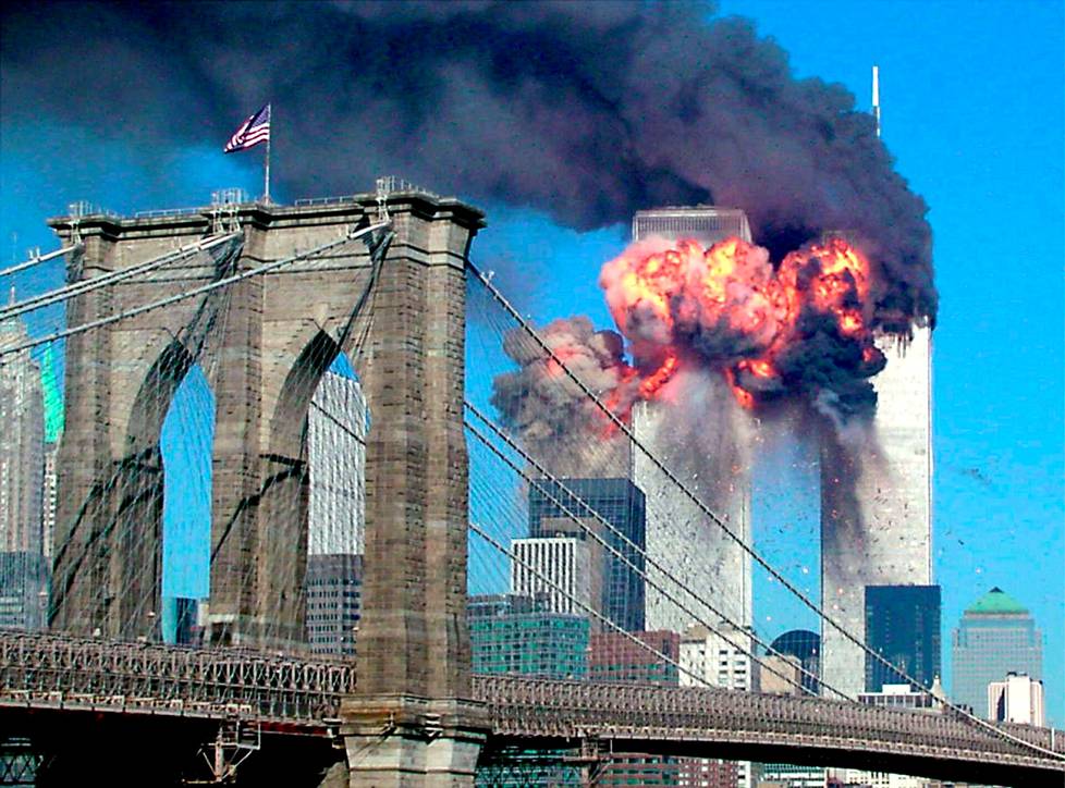 Eteläinen World Trade Center -torni syttyy rajuihin liekkeihin sen jälkeen, kun sitä päin on lentänyt kaapattu matkustajakone 11. syyskuuta vuonna 2001 New Yorkissa, Yhdysvalloissa. Pohjoiseen torniin on törmännyt toinen kaapattu kone hetkeä aiemmin. Sankka savu leviää Manhattanin ylle. Kuvan etualalla näkyy Brooklynin silta.